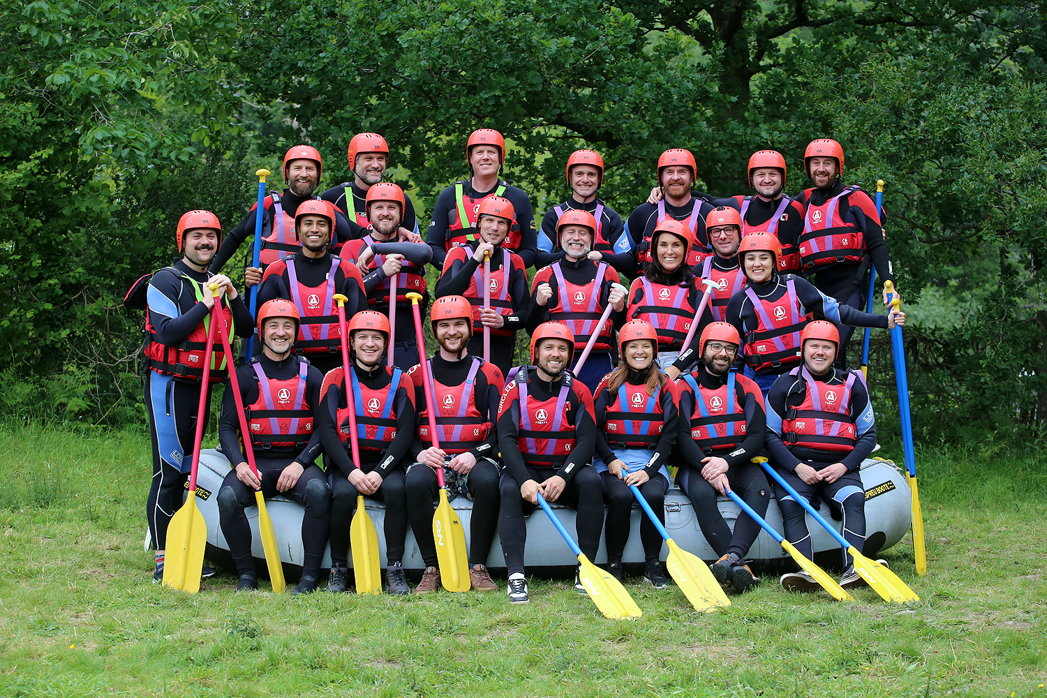 Uniform team posing with helmets, life jackets and paddles before rafting